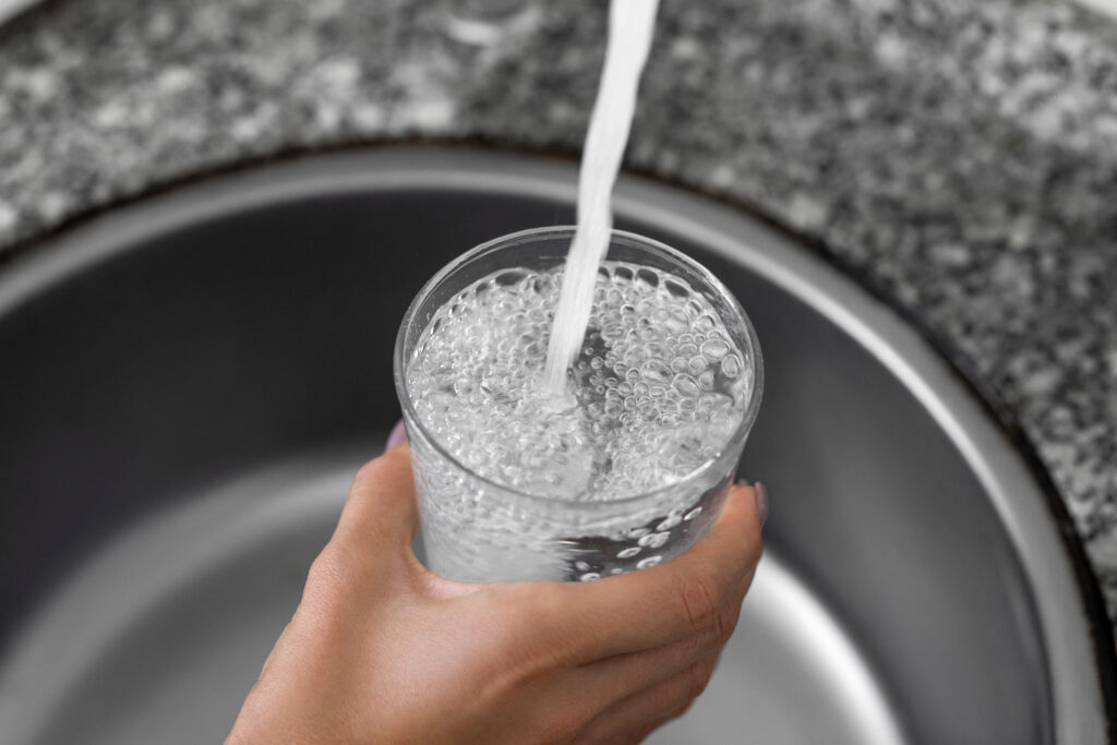 Unrecognizable female hands pouring tap water into a glass from a faucet