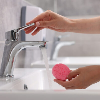 Young woman washing face sponge in bathroom, closeup